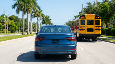 A car hire stops for a yellow school bus with its lights flashing on a sunny street in Orlando
