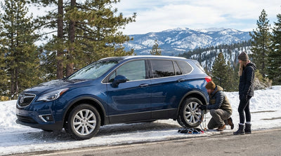 A car hire drives on a winding road through a snow-covered pine forest in the mountains of California