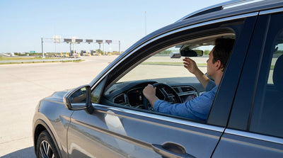 A white car rental driving under an electronic toll gantry on a sunny Texas highway