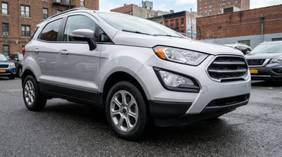A driver inspects the tire tread of a silver car rental parked on a city street in New York