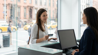 A person's hand holding a credit card to pay for a car hire with a yellow New York City taxi in the background