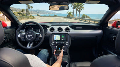 A car rental dashboard with Android Auto navigating a sunny coastal highway in California
