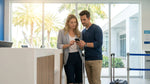 Customer checking a watch at a car rental desk with a sunny Miami street visible outside