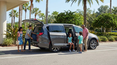 A family loading their 8-passenger car rental van on a sunny suburban street with palm trees in Orlando