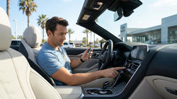 Hand pressing a dashboard start button inside a car rental with sunny California palm trees visible outside
