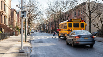 A yellow school bus with flashing lights stopped on a street in New York, seen from a car hire vehicle