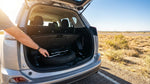 A person inspects the spare tire in the trunk of a car rental under the bright Texas sun