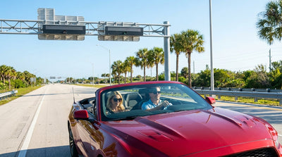 A car rental driving under an electronic toll gantry on a sunny highway in Florida lined with palm trees