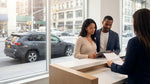 Person signing car hire paperwork at a desk with a New York City street view through the window