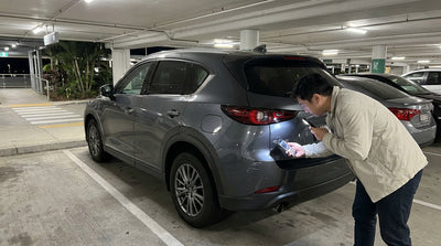 A person uses a phone flashlight to inspect their Orlando car hire for damage in a dark airport parking garage