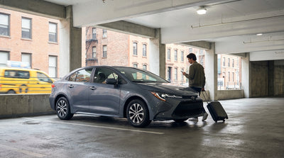 A white car rental driving through a busy Times Square intersection with classic yellow cabs in New York City