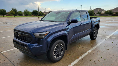 A car rental with visible hail damage on its hood parked under a stormy Texas sky