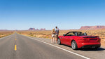 A family driving their car rental past a painted Route 66 sign on a desert highway