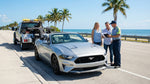 A silver car hire is pulled over with hazard lights on beside a sunny, palm-lined highway in Florida
