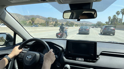 View from a car rental of a motorcycle lane-splitting through traffic on a sunny California freeway