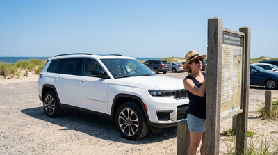 A silver car hire parked in a sunny beach parking lot on Long Island, New York, near the ocean dunes