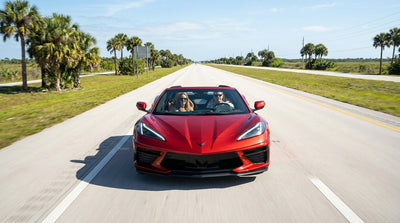 A convertible car hire driving down a scenic Florida highway lined with tall palm trees under a bright blue sky