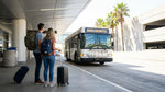 Passengers with luggage walking toward a car rental shuttle bus outside the Las Vegas airport terminal