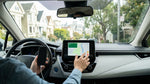 A driver's hands setting up navigation on a car rental dashboard screen with a San Francisco street in the background