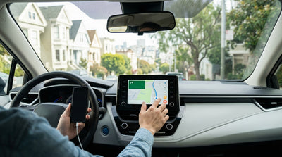 A driver's hands setting up navigation on a car rental dashboard screen with a San Francisco street in the background