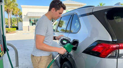 A person holding a fuel pump nozzle to the open fuel tank of their Florida car hire at a sunny gas station
