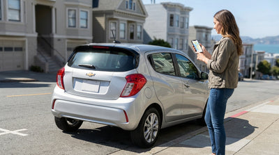 A person using a smartphone next to their car rental on a sunny, hilly street in San Francisco