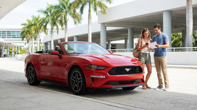 A modern car rental driving on a highway over the water with the sunny downtown Miami skyline in the background
