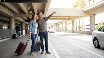 Travelers with luggage waiting for a car rental shuttle at the curb of LAX Terminal 1 in Los Angeles