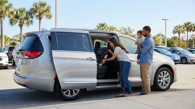 A father installs a child seat into the back of a Florida car hire sedan as his family watches on