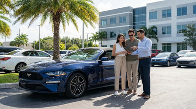 A white convertible car rental driving along Ocean Drive in Miami with sunny art deco hotels and palm trees in the background