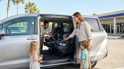 A happy family with young children loading luggage into their car rental SUV in Florida