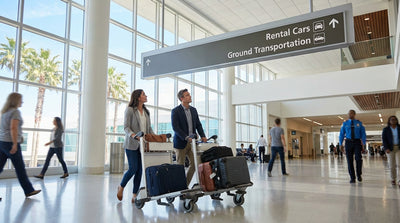 A traveler with luggage looking at an overhead sign for the car rental shuttle bus inside the LAX airport in Los Angeles