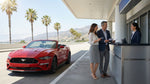 A red convertible car hire driving on a sunny, winding coastal road in California