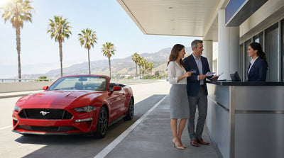 A red convertible car hire driving on a sunny, winding coastal road in California