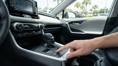 A person's hand pressing the electronic brake button in a modern car hire with a sunny Orlando street in the background