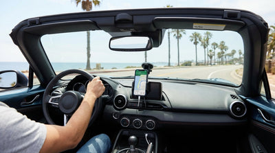 A phone in a dashboard mount inside a car rental driving along a sunny California highway with palm trees