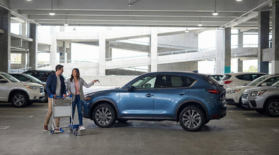 A purple LAX shuttle bus for car hire services parked outside a busy Los Angeles airport terminal