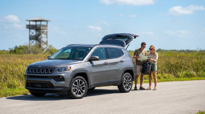 A white convertible car hire driving down a sun-drenched Miami road lined with tall, green palm trees and a clear blue sky
