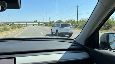 A car rental driving on a frontage road running parallel to a multi-lane highway in sunny Texas