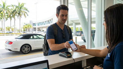 A customer uses a smartphone for a contactless payment at a car hire counter in Miami