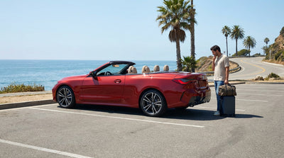 A white SUV car hire parked at a scenic viewpoint overlooking the Pacific Ocean on a sunny day in California