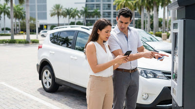 A shiny sedan used for car hire is parked on a sunny street with palm trees and a parking meter in Miami