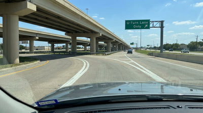 A modern car hire driving on a wide Texas highway with a complex interchange of overpasses ahead