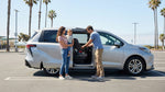 A parent installs a child car seat in the back of a modern car rental on a sunny day in California