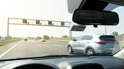 A silver car rental passing through an E-ZPass toll plaza on a busy highway in New York