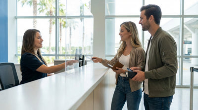 A driver places luggage into the trunk of a white sedan car rental in a sunny Orlando airport parking lot