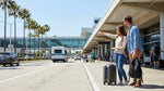 A purple and white car rental shuttle bus waits for passengers on the arrivals curb at LAX in Los Angeles