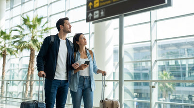 Travelers with luggage wait under the purple car rental shuttle sign at LAX airport in Los Angeles