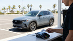 A person holds a credit card and keys for their car hire on a sunny, palm-lined road in California