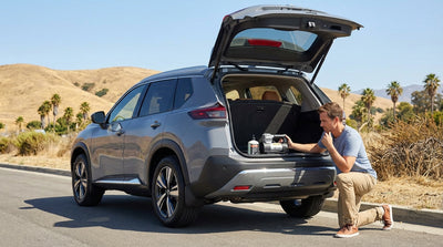 A driver inspects a flat tire on their car hire on the side of a sunny California highway